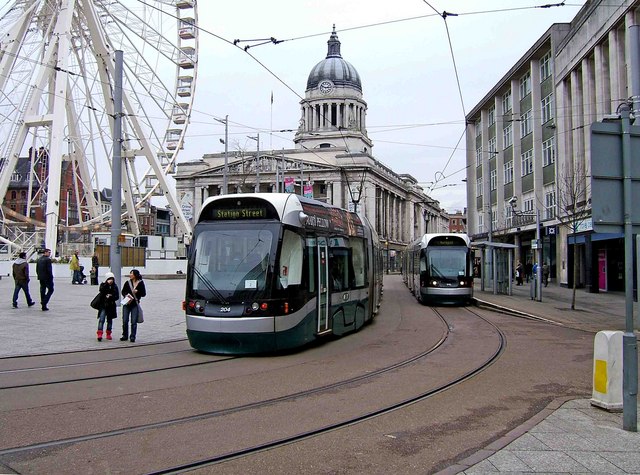 Two trams on tram lines in Nottingham city centre, there is an old building and a large ferris wheel in the background