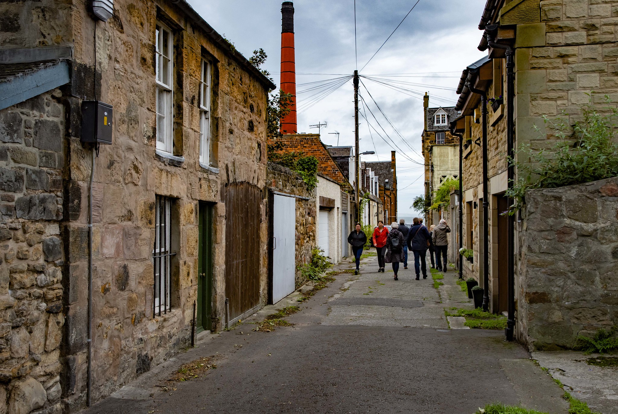 A group of adults walk along a narrow, carless street between some old buildings