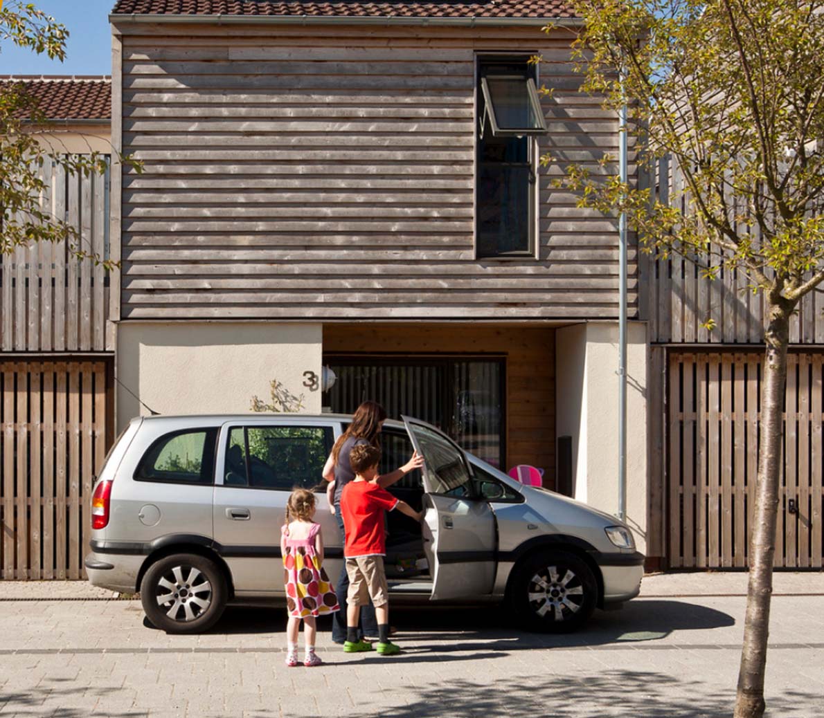 family getting into a car outside of a modern house with a wooden design