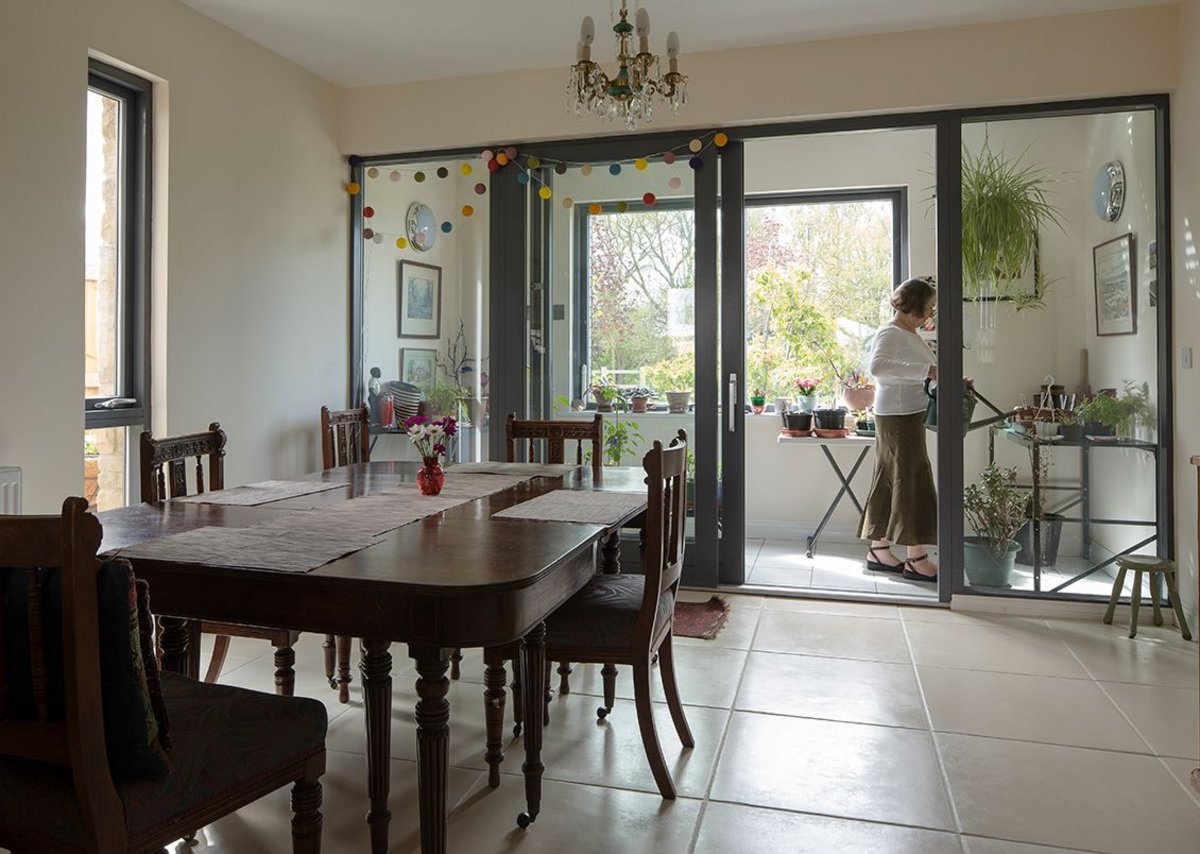 A photo of a dining space in a house at Derwenthorpe. Some french doors go through to a 'sun room' where a resident waters their plants