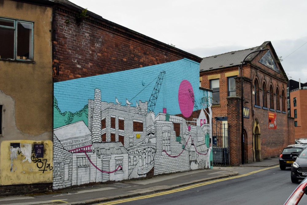 Street art on a red brick building. The street art shows an urban scene, with a bright blue sky